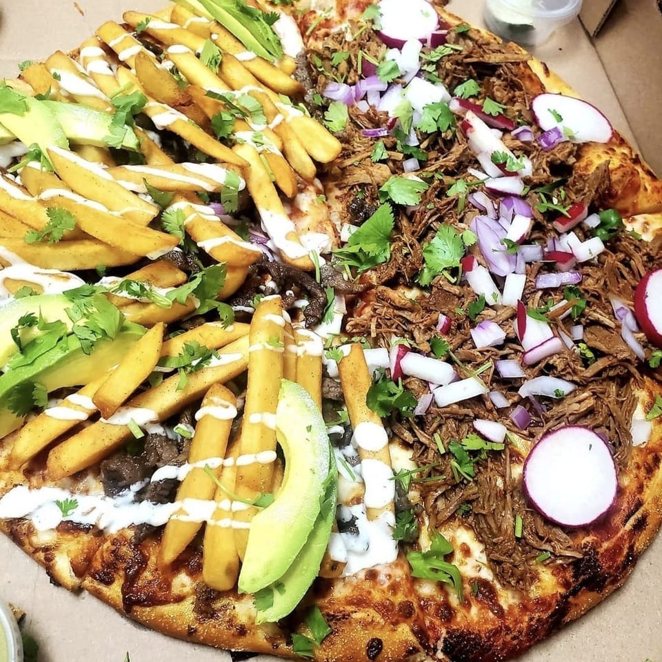 Loaded pizza topped with fries, shredded meat, avocado, radishes, red onion, cilantro, mushrooms, and white sauce.