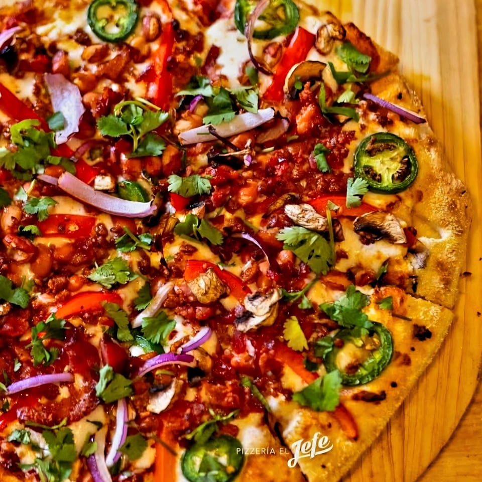 Loaded pizza topped with melted cheese, jalapeños, mushrooms, red onions, peppers, tomato sauce, and fresh cilantro on a wooden board.